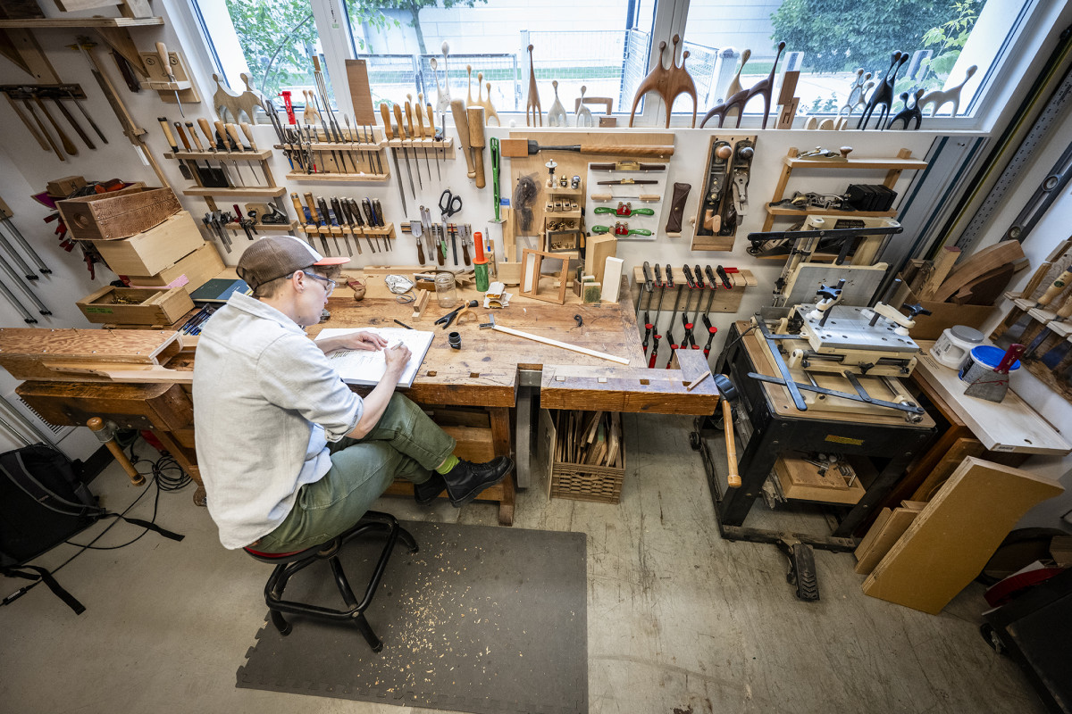 A person sketching in a wood shop surrounded by tools