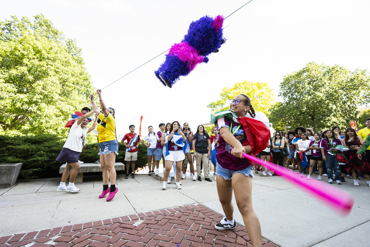 A person swinging a bat at a pinata with a smiling audience behind them