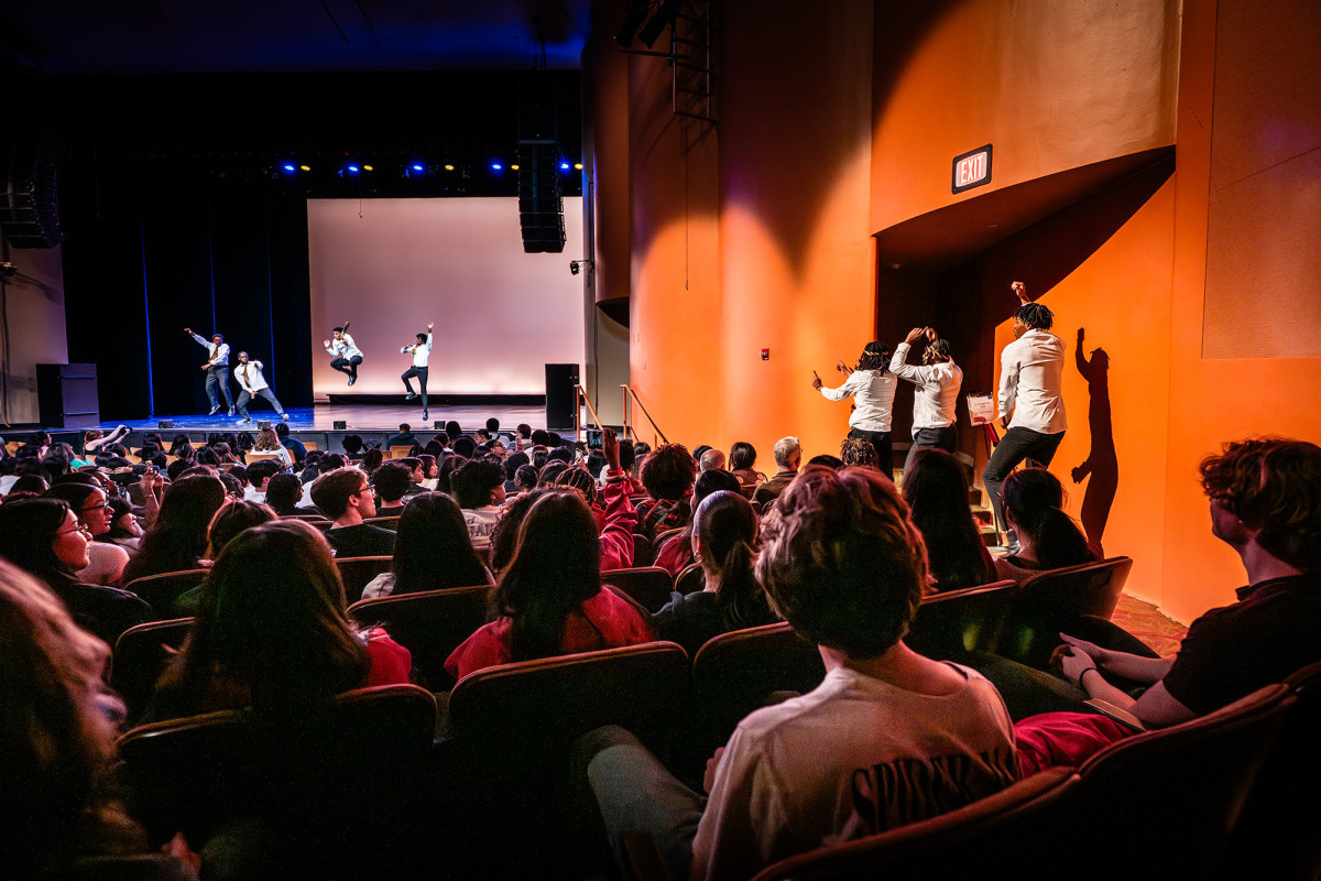 Performers on a stage and in the aisle with audience members looking on