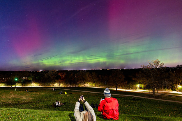 Several groups of people sitting on hillside while observing the Northern Lights in the night sky