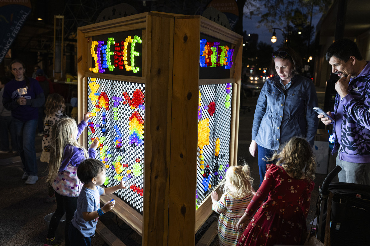 Children and adults gathered around a giant "Light Bright" display, adding colorful pegs