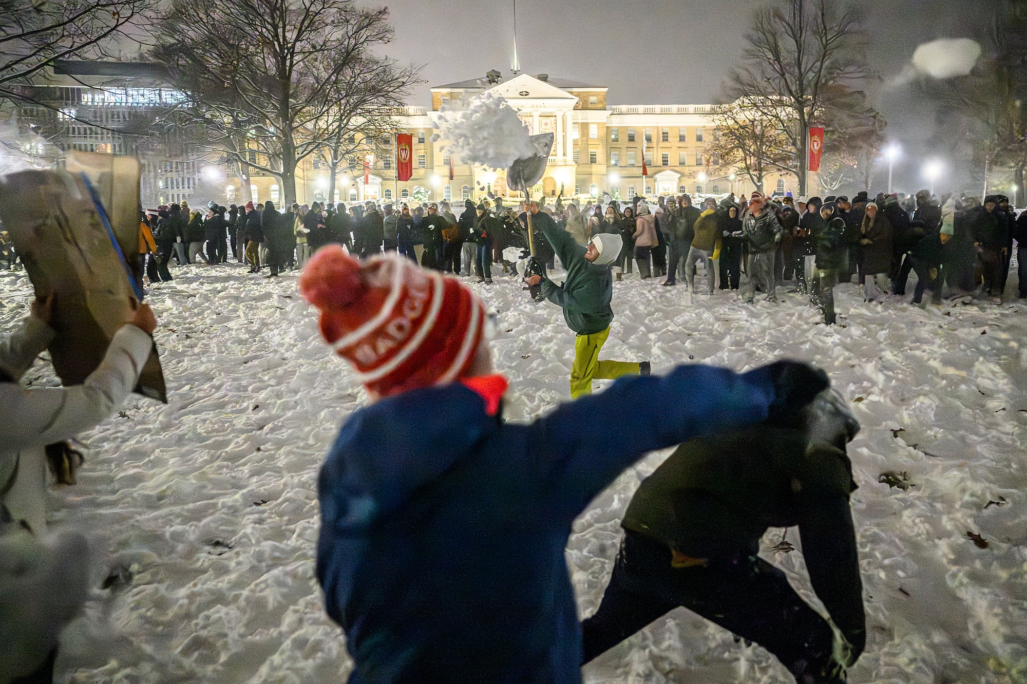 Hundreds of students- including a student using a snow shovel- throwing snow with Bascom Hall in the background