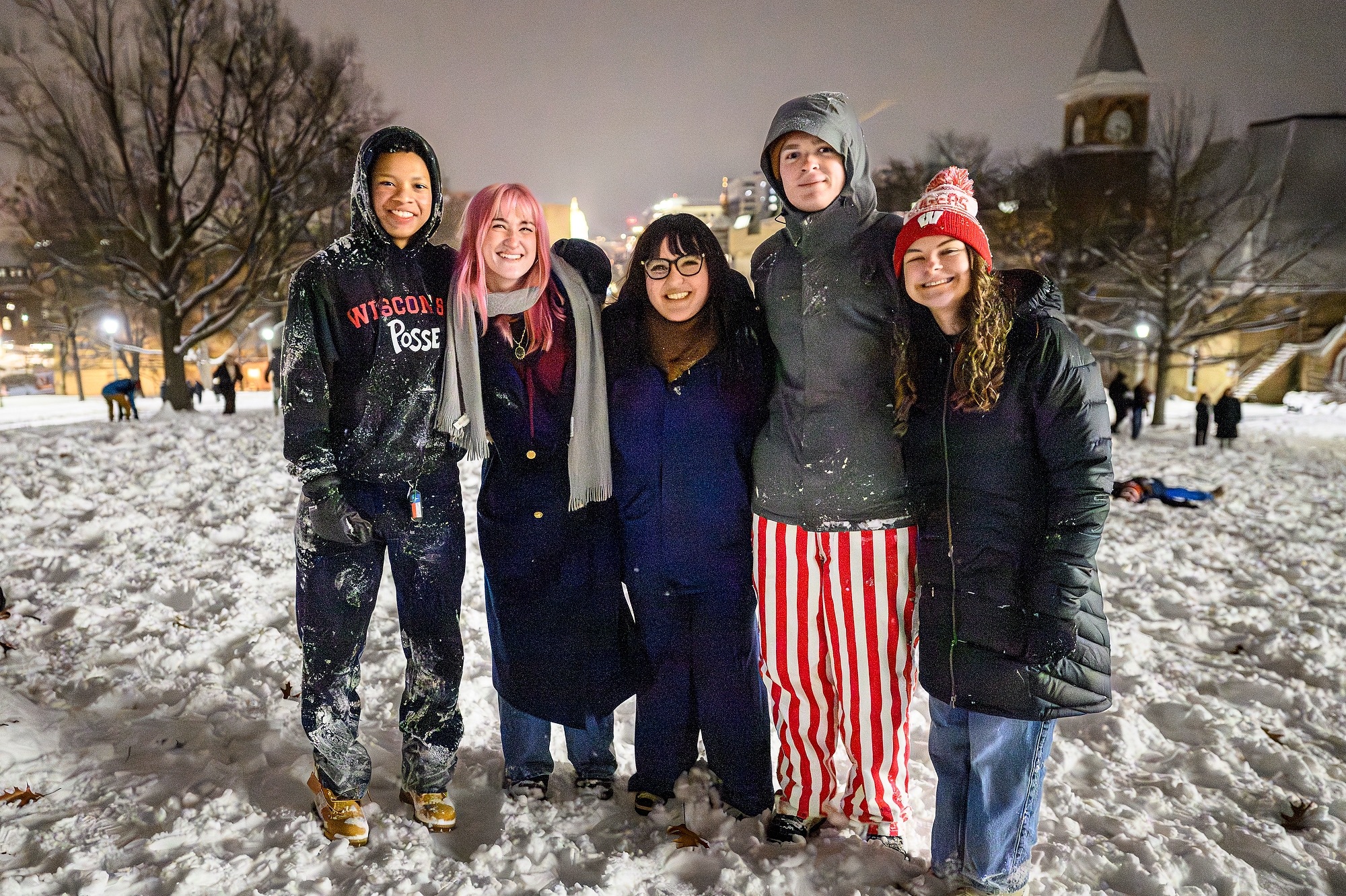 A group of five students smiling for a photo on a snowy Bascom Hill. Music Hall and the Wisconsin State Capitol can be seen in the distance.