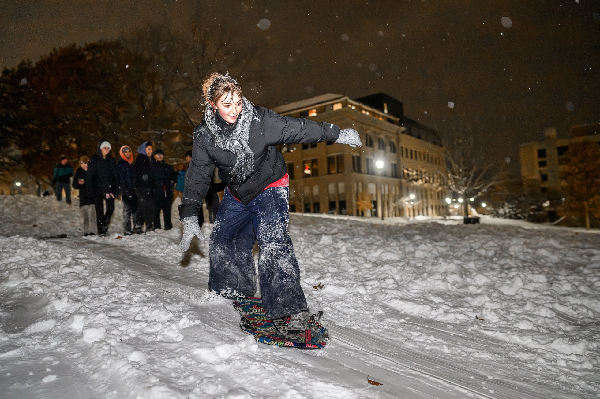 A students standing on a sled to ride down snowy Bascom Hill