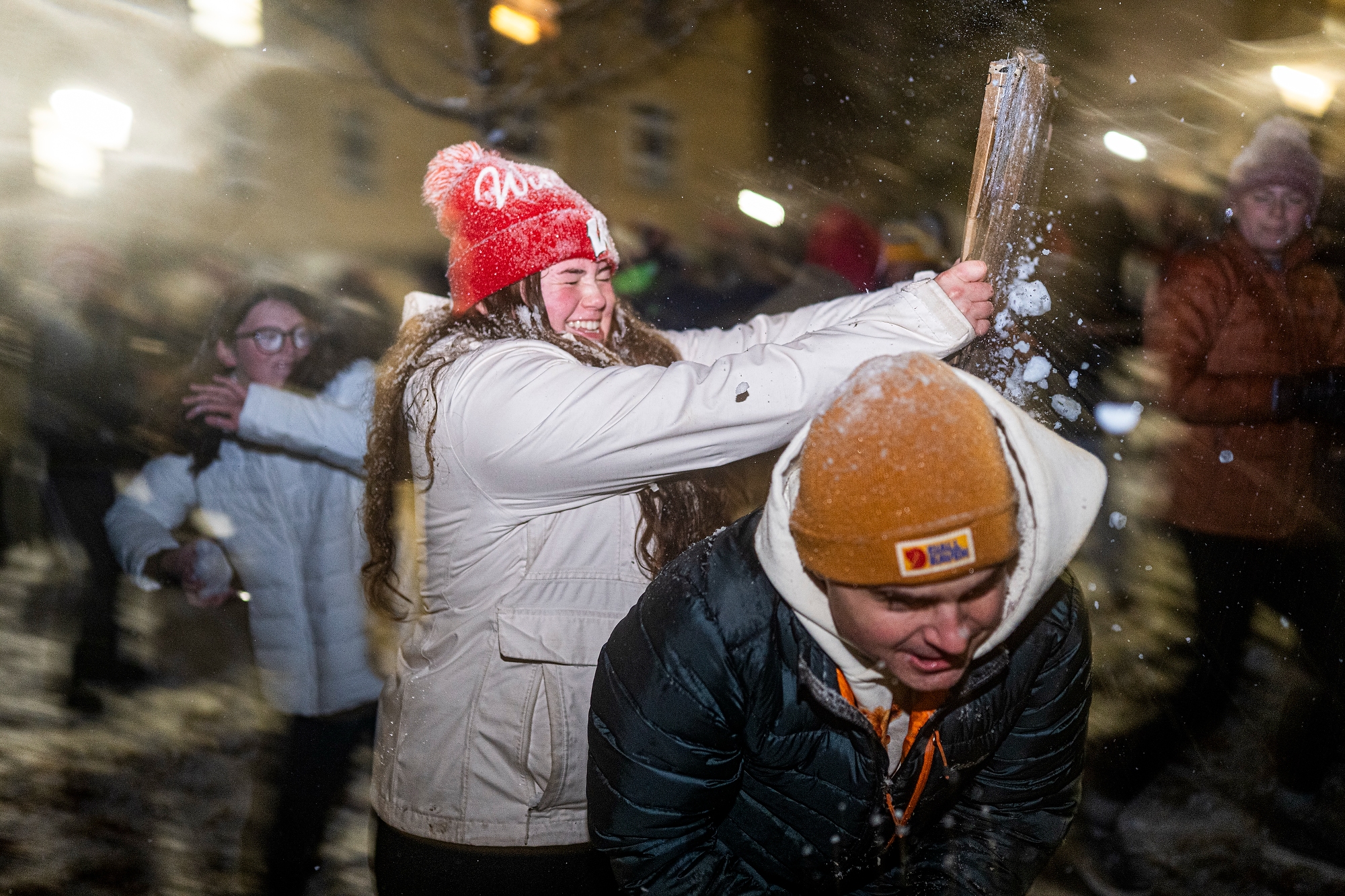 Student in a red Wisconsin hat blocking a snowball with a cardboard shield