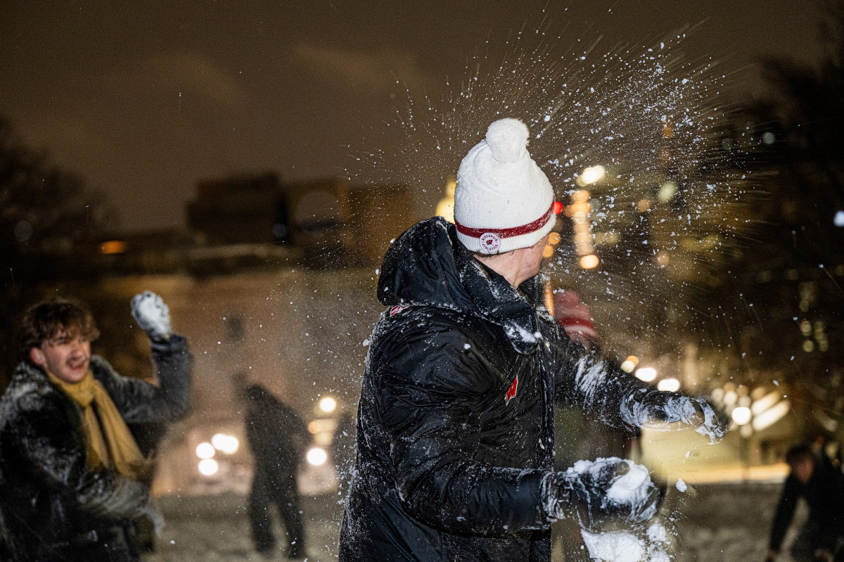 Snow crashing against the jacket of a student wearing a Wisconsin Athletics hat