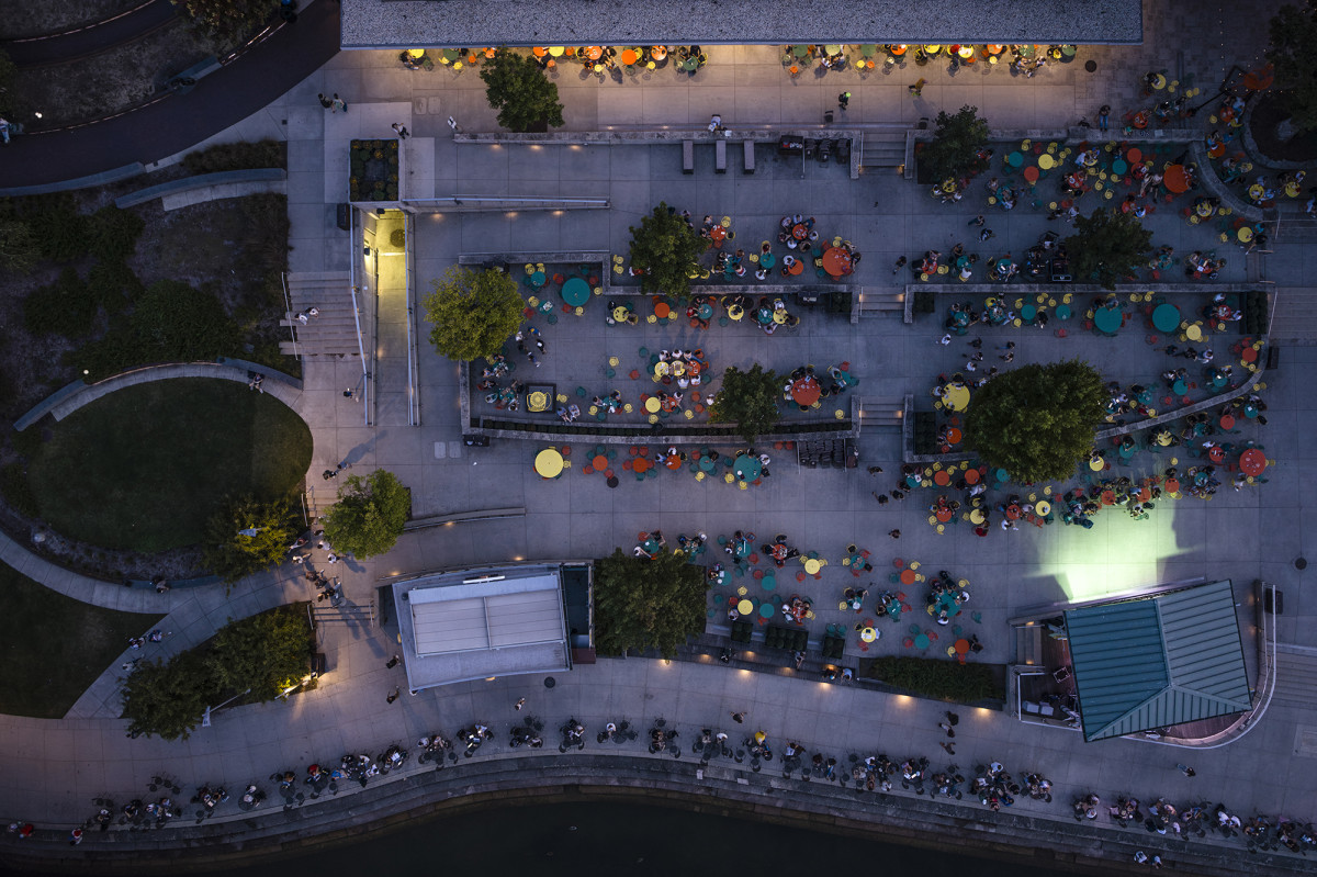 Drone view of colorful tables on a terrace with people sitting around them