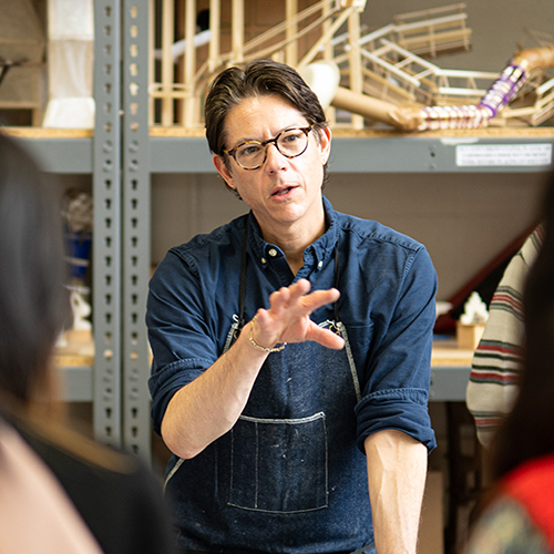 A professor talking to a group of students with artwork on shelves in the background