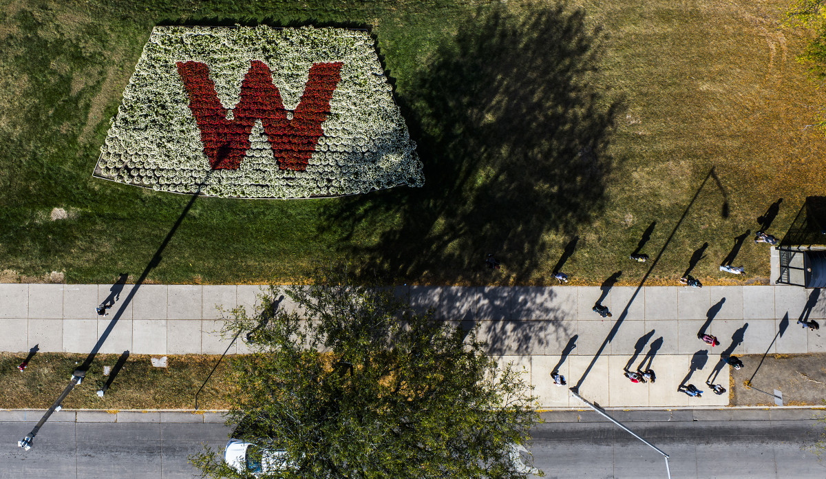 Drone view of a flower bed with a "W" made of flowers and people walking on the sidewalk