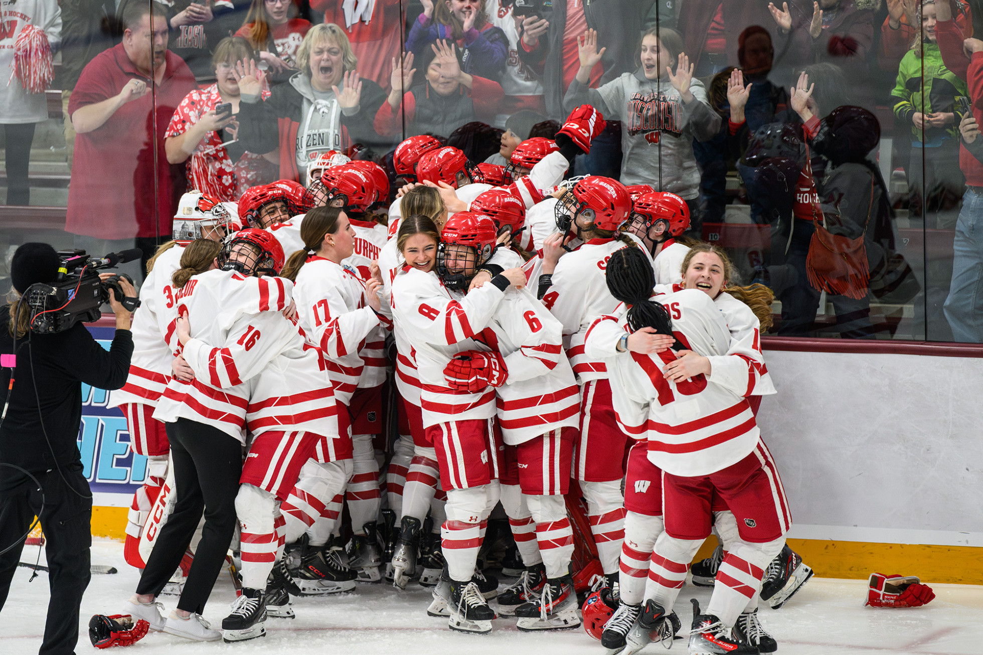 Group of hockey players hugging and smiling while fans cheer at the glass behind them