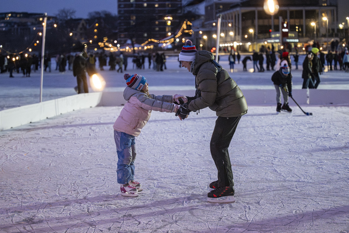 A child and an adult holding hands and smiling at each other while ice skating
