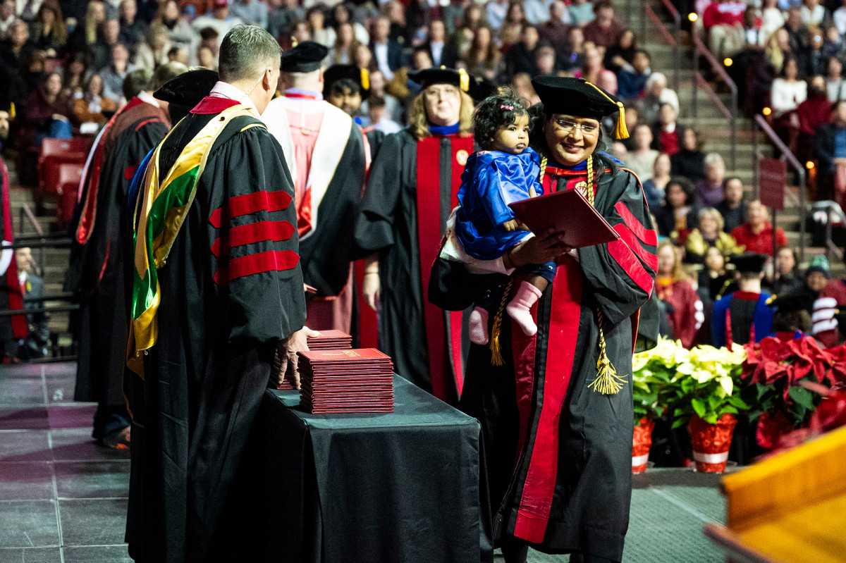 A graduate crosses the stage holding her diploma in one arm and her baby daughter in the other.