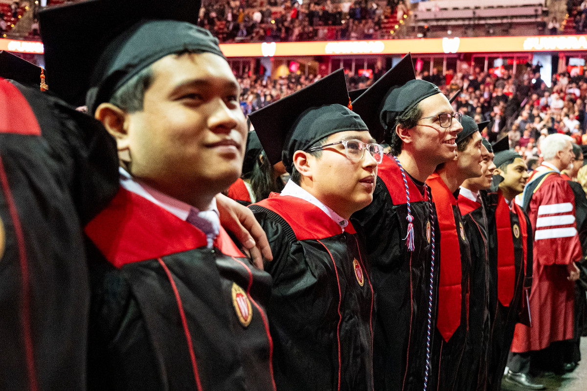 Graduates stand with their arms around each others' shoulders as they sway to the tune of Varsity