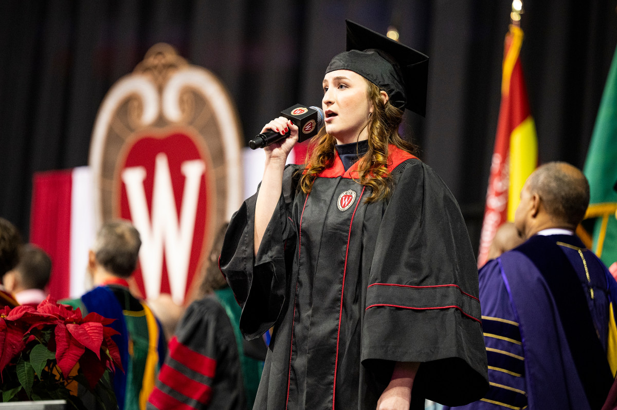 A graduate stands and sings the National Anthem.