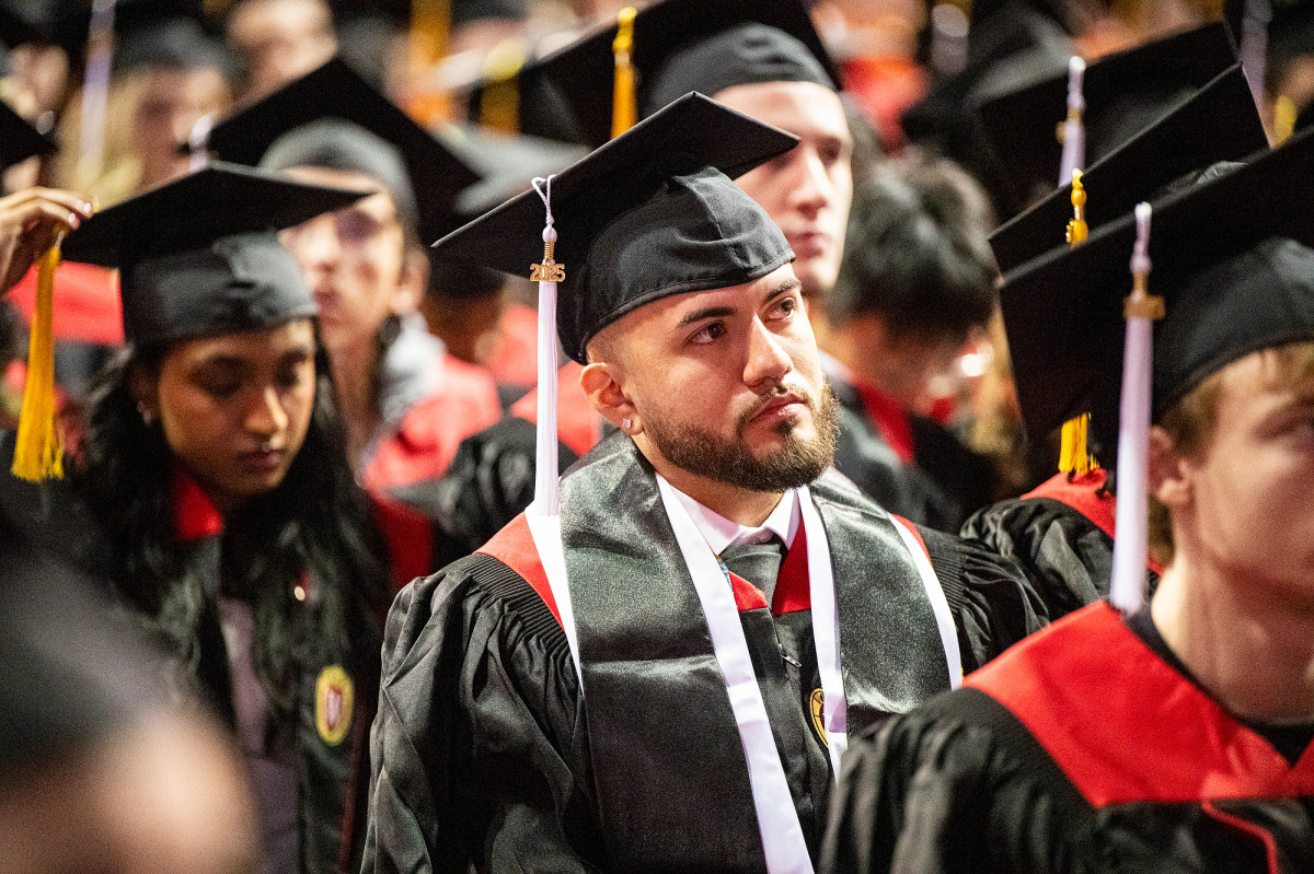 Graduates in caps and gowns listen intently to a speaker.