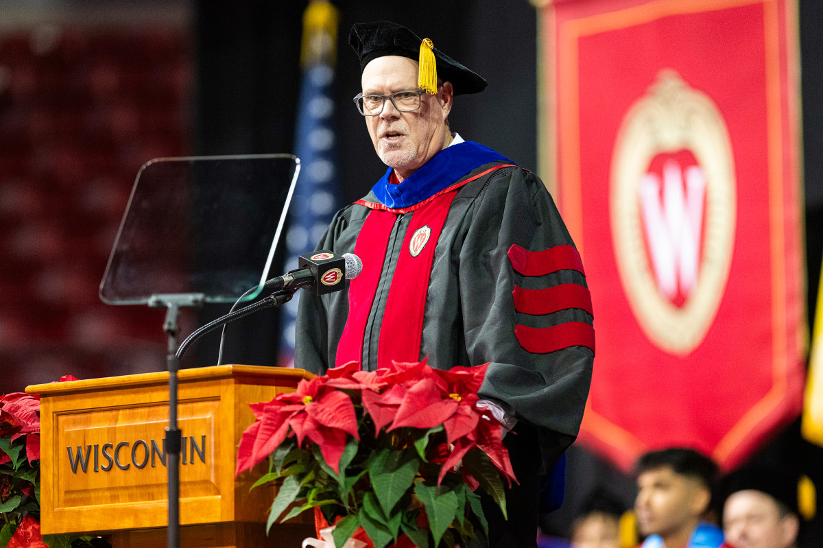 A man wearing academic regalia speaks from a podium.