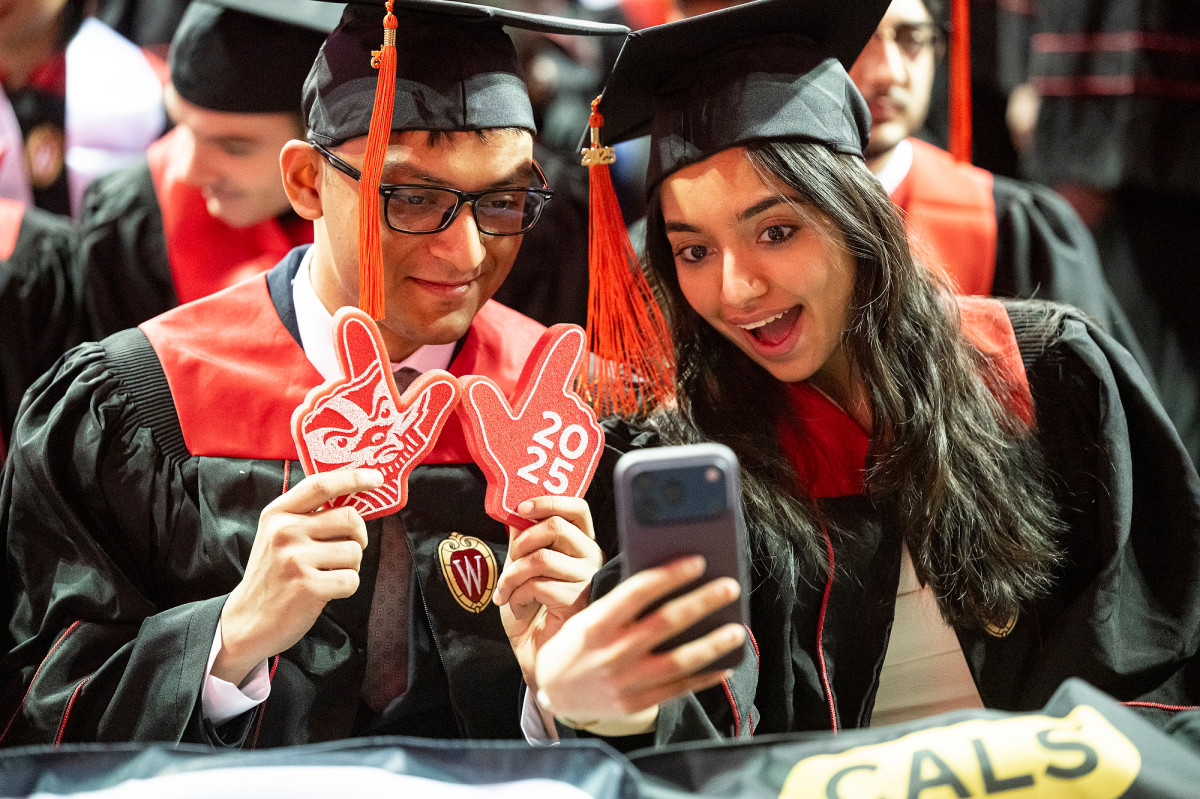 Two graduates lean their heads together to check a selfie.