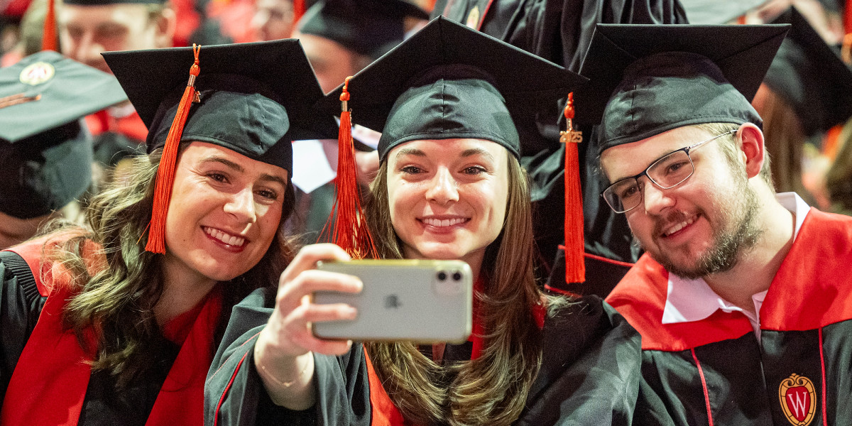 Three graduates in academic regalia lean together to take a selfie.