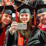 Three graduates in academic regalia lean together to take a selfie.
