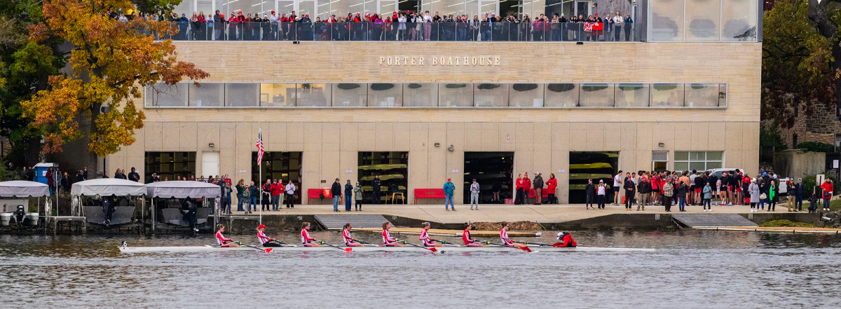 Members of a crew team rowing on a lake with spectators watching from land