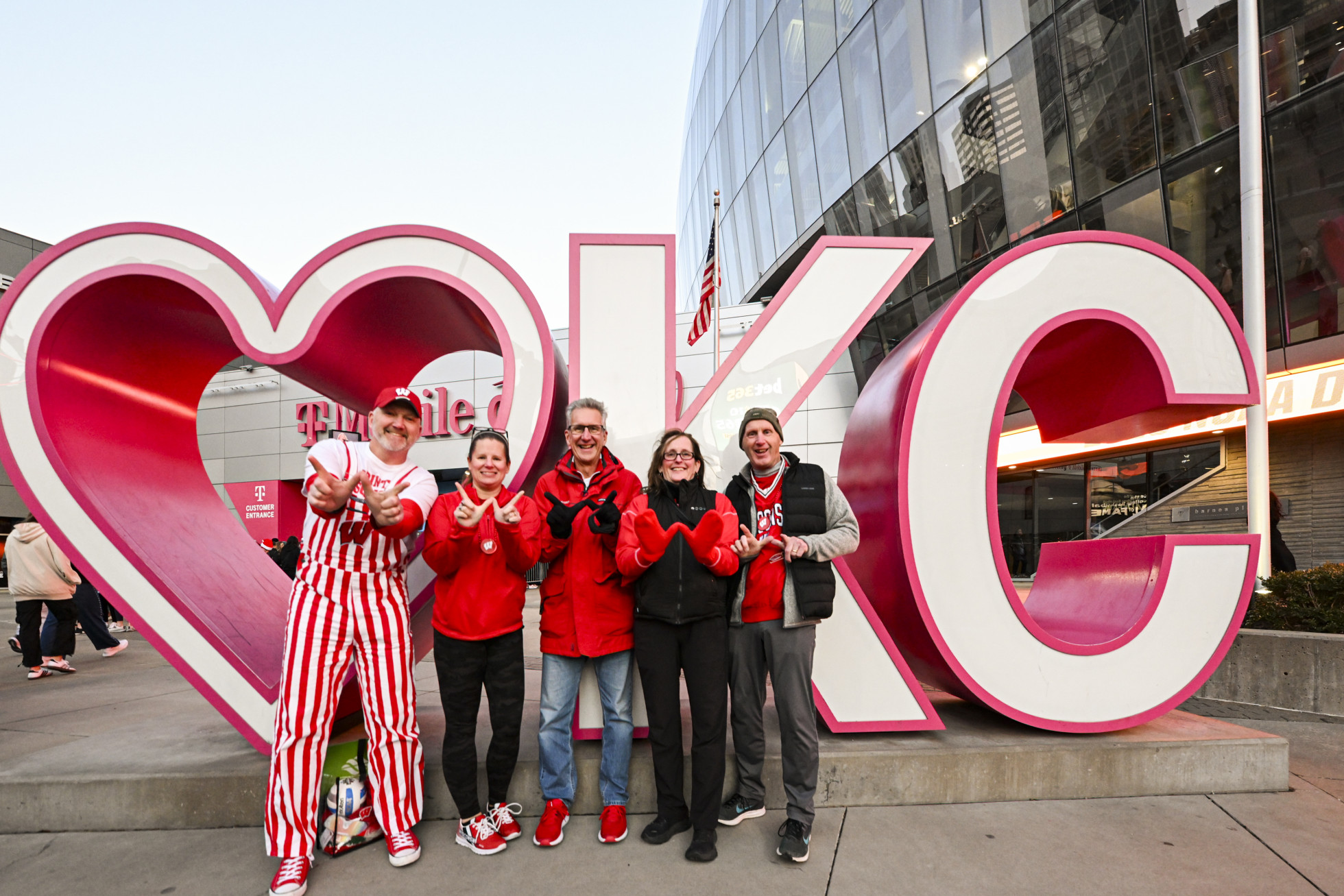 Badger fans flash Ws with their hands while standing in front of a "heart OKC" sign.