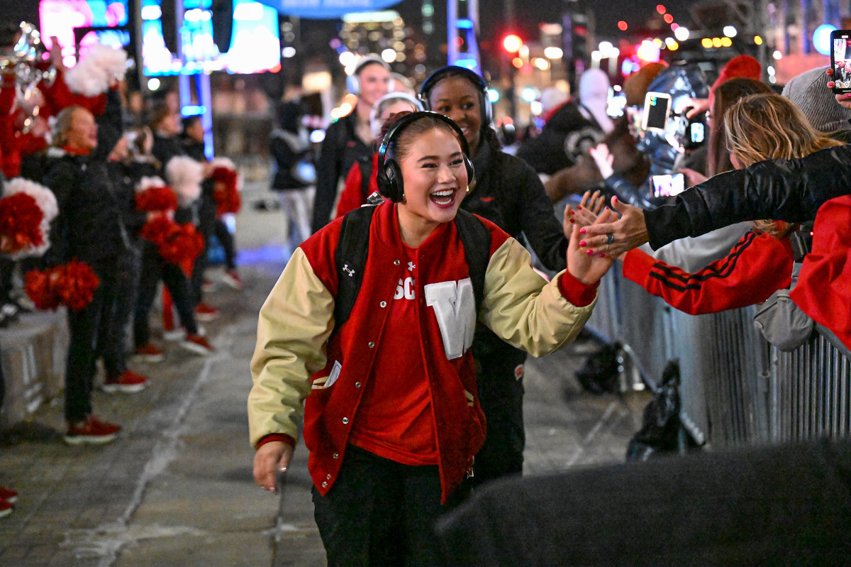 Volleyball player Maile Chan, wearing a W varsity jacket, high fives fans outside T-Mobile Stadium.