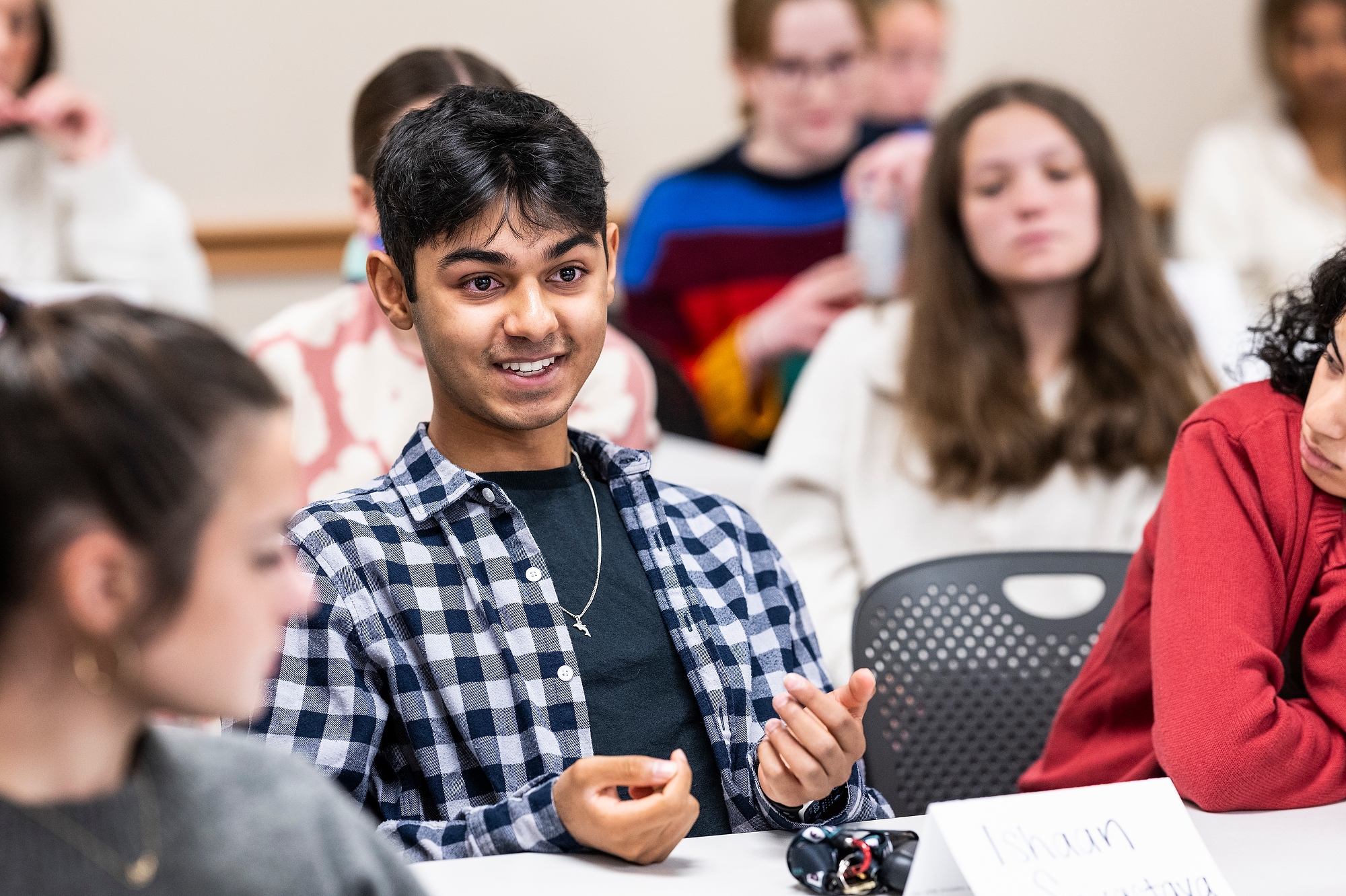 Srivastava speaks to classmates sitting at his table in a classroom.