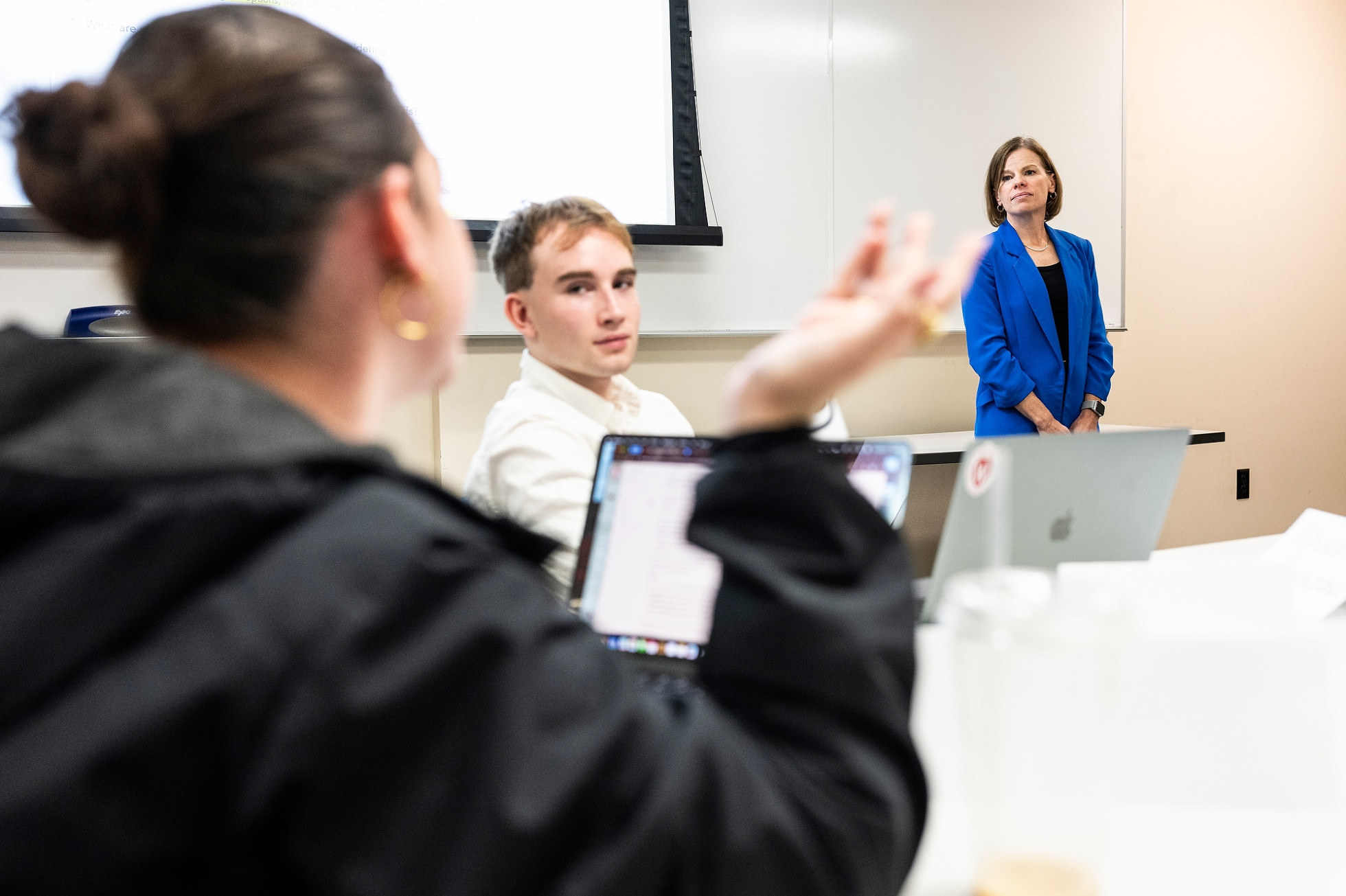 Wichowsky stands at the front of the classroom and listens to a student speaking during the class.