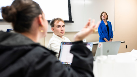 Wichowsky stands at the front of the classroom and listens to a student speaking during the class.