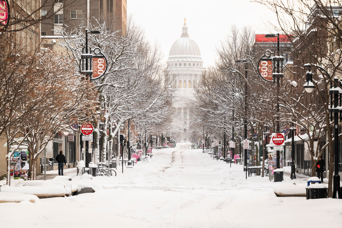 A look down Madison's State Street, with stores and trees lining it and the white dome of the state capitol at the end of it. Pedestrians walk on the sidewalk.