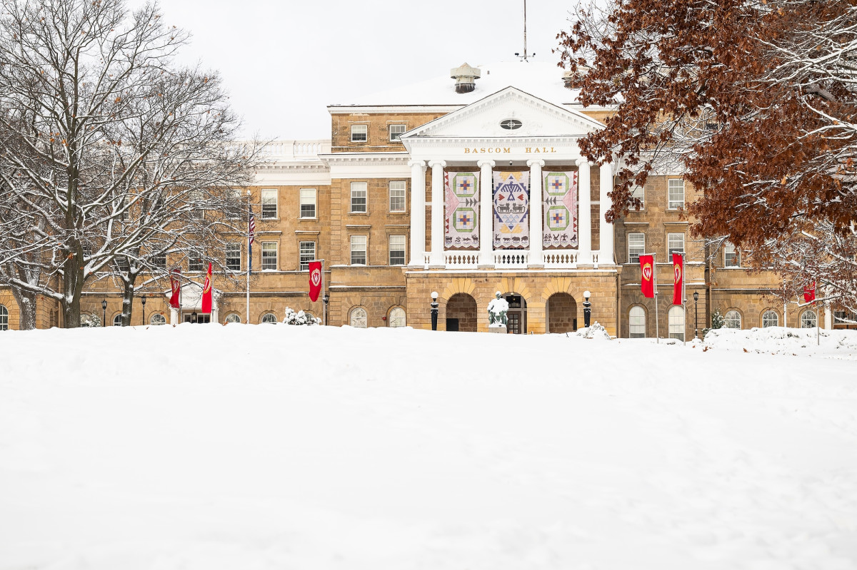 A large stone building with white pillars is pictured - the lawn in front of it is snow-covered, and large banners hang from its exterior.