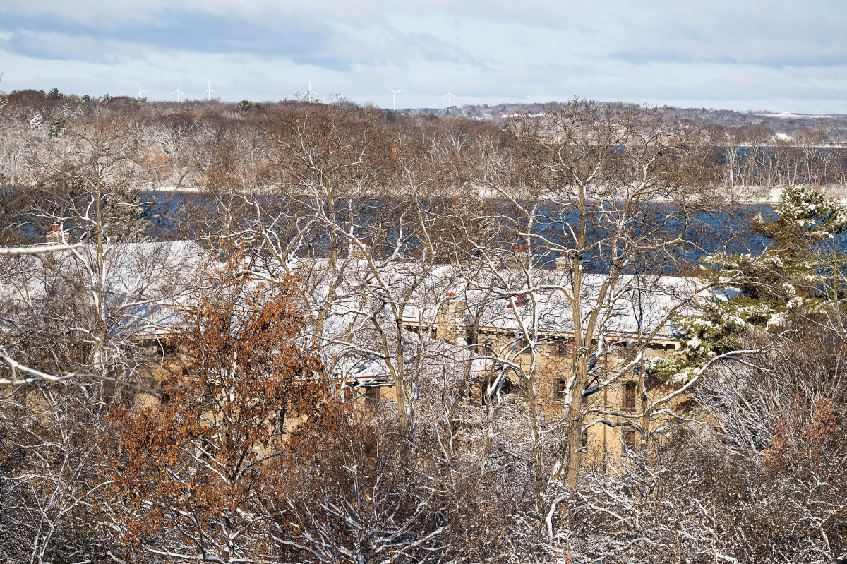 A landscape photo showing trees, a stone building, a lake and a peninsula. All is covered in snow.