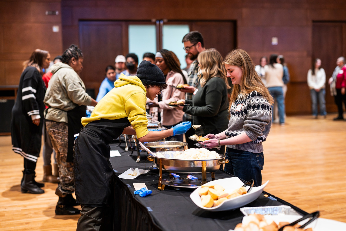 Event attendees line a buffet table as event hosts serve them food.