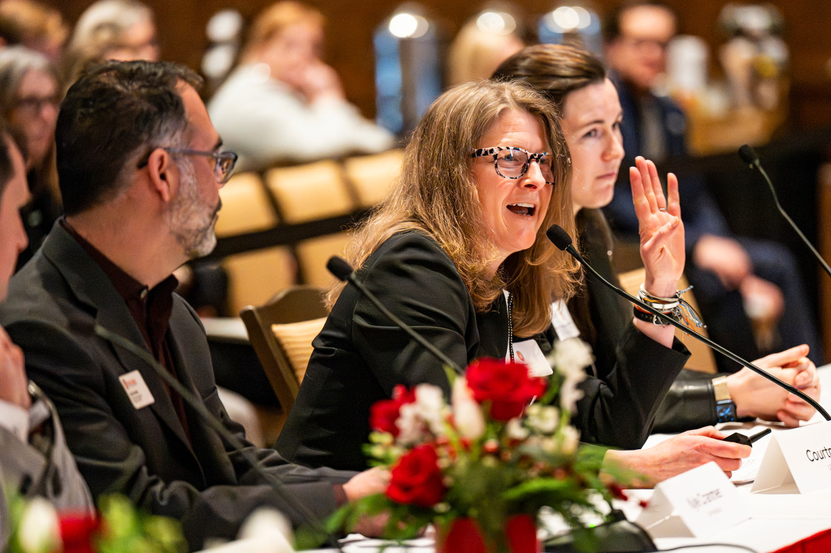 A woman sits on a panel on a stage and speaks.