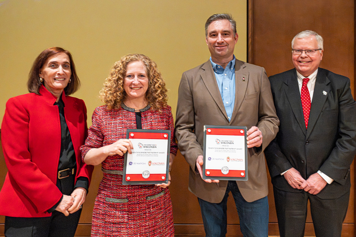 Four people stand in a row posing for the camera, with the middle two holding up an award.