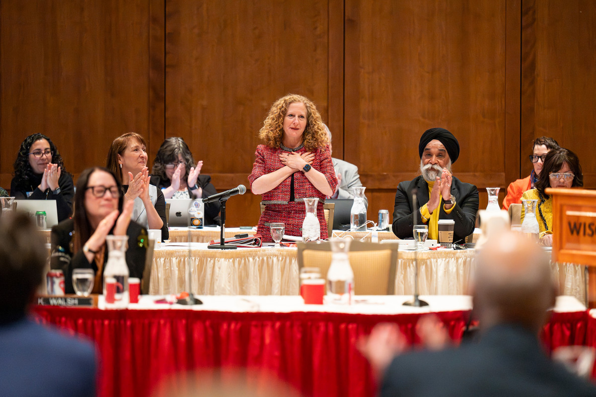 A woman stands at a podium, holding her hands together in a position of happiness and gratitude.
