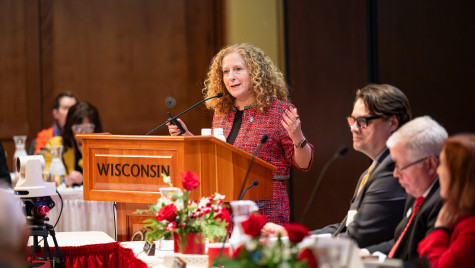 A woman stands at a podium and talks and gesticulates as others listen.