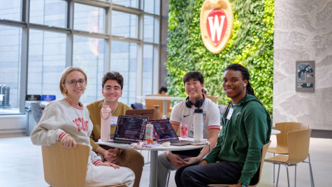 Four students sit around a table and smile at the camera during their collaborative project session.