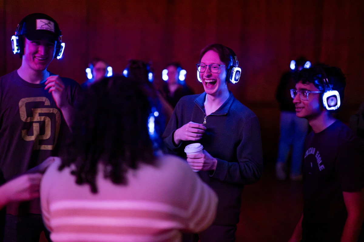 In a room lit with a dim purple light students dance.
