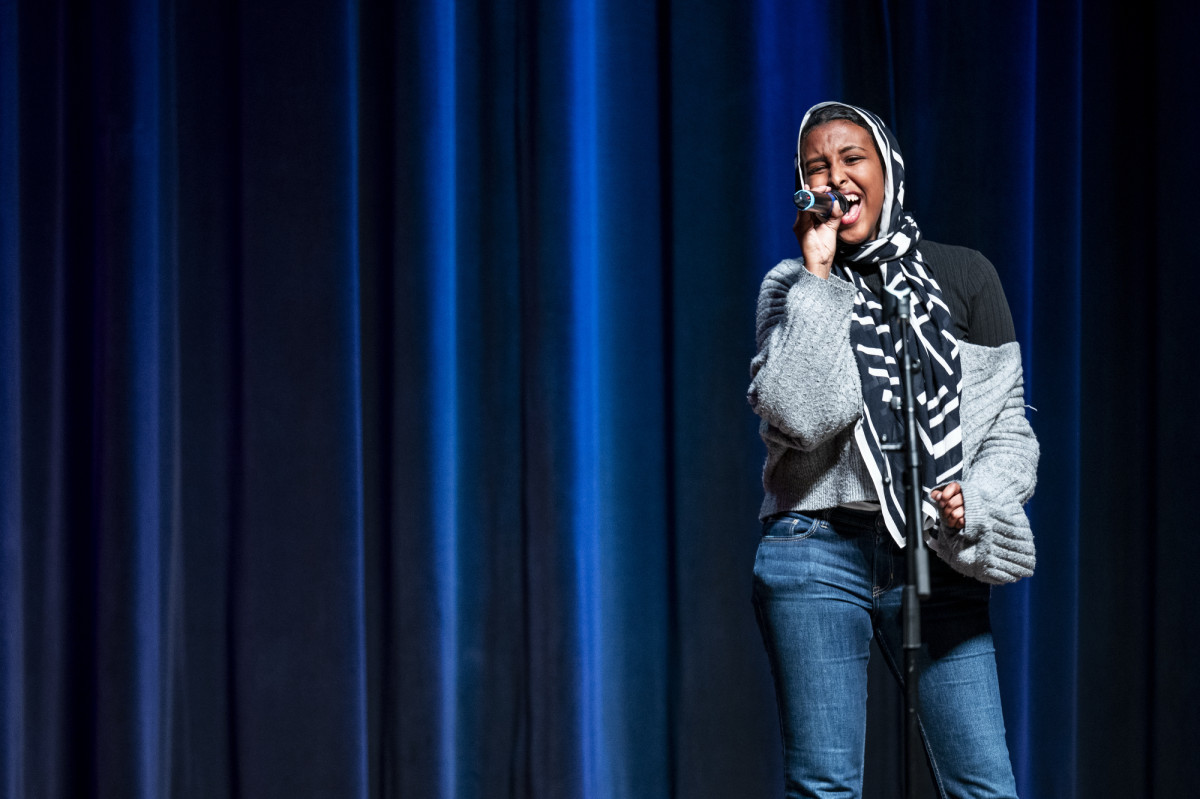 A student holds a microphone on stage and sings.