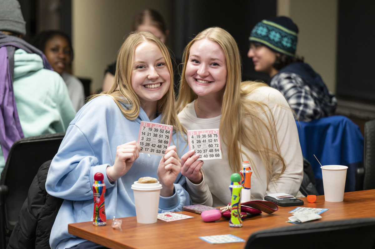 Two young women sit at a table playing bingo.