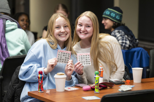 Two young women sit at a table playing bingo.