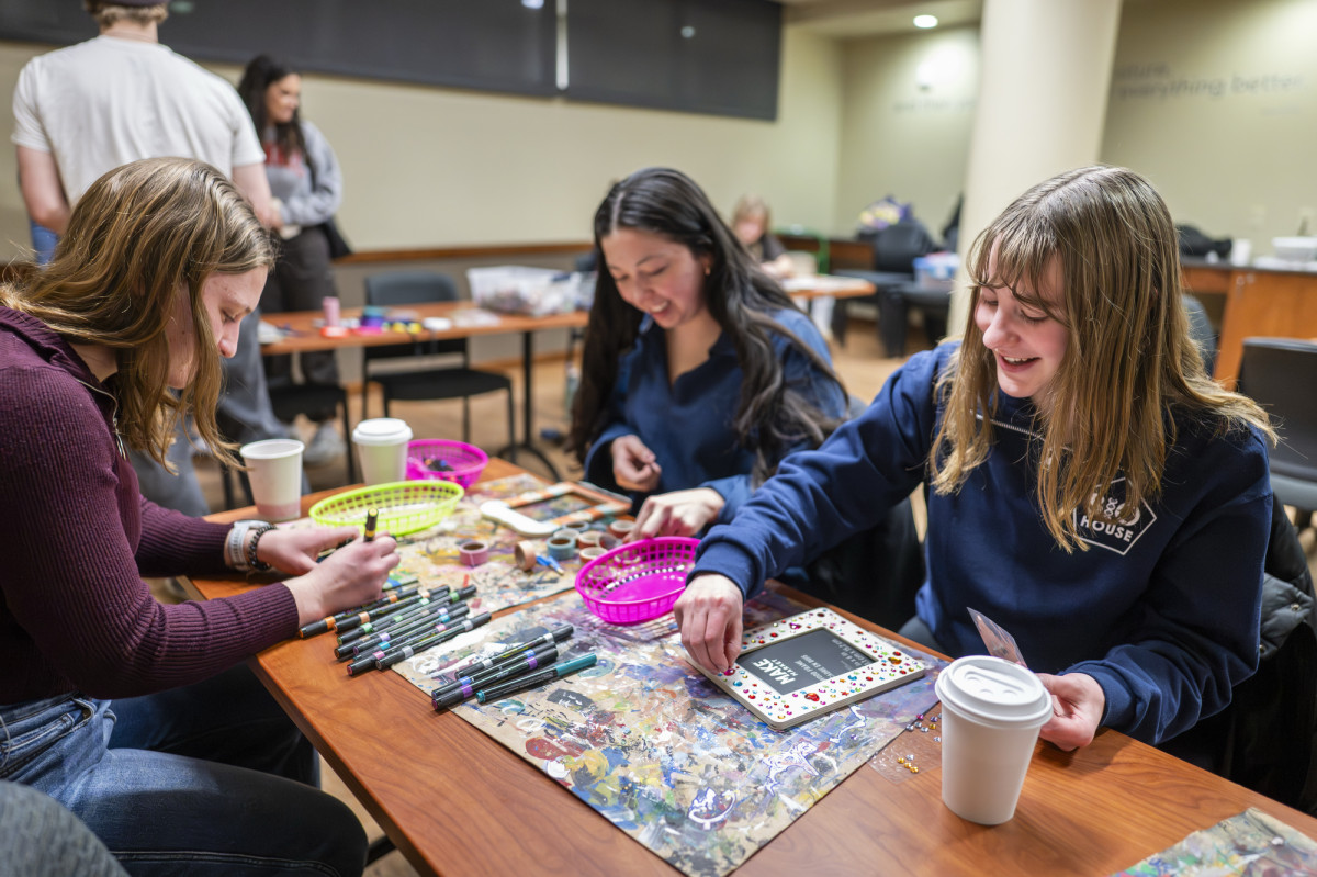 Students gather around a table and create art.