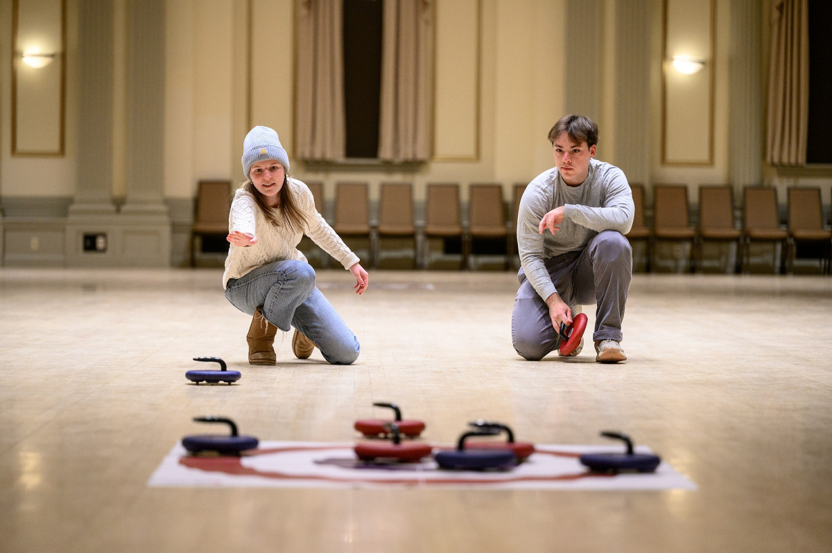 At left, a woman throws a curling stone toward the target as a man looks on during the “Floor Curling with RecWell Intramurals” event in Great Hall at the Memorial Union.