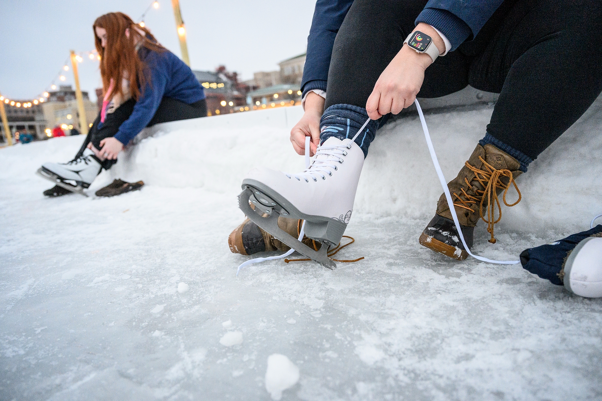 Two people's sit and lace up ice skates.