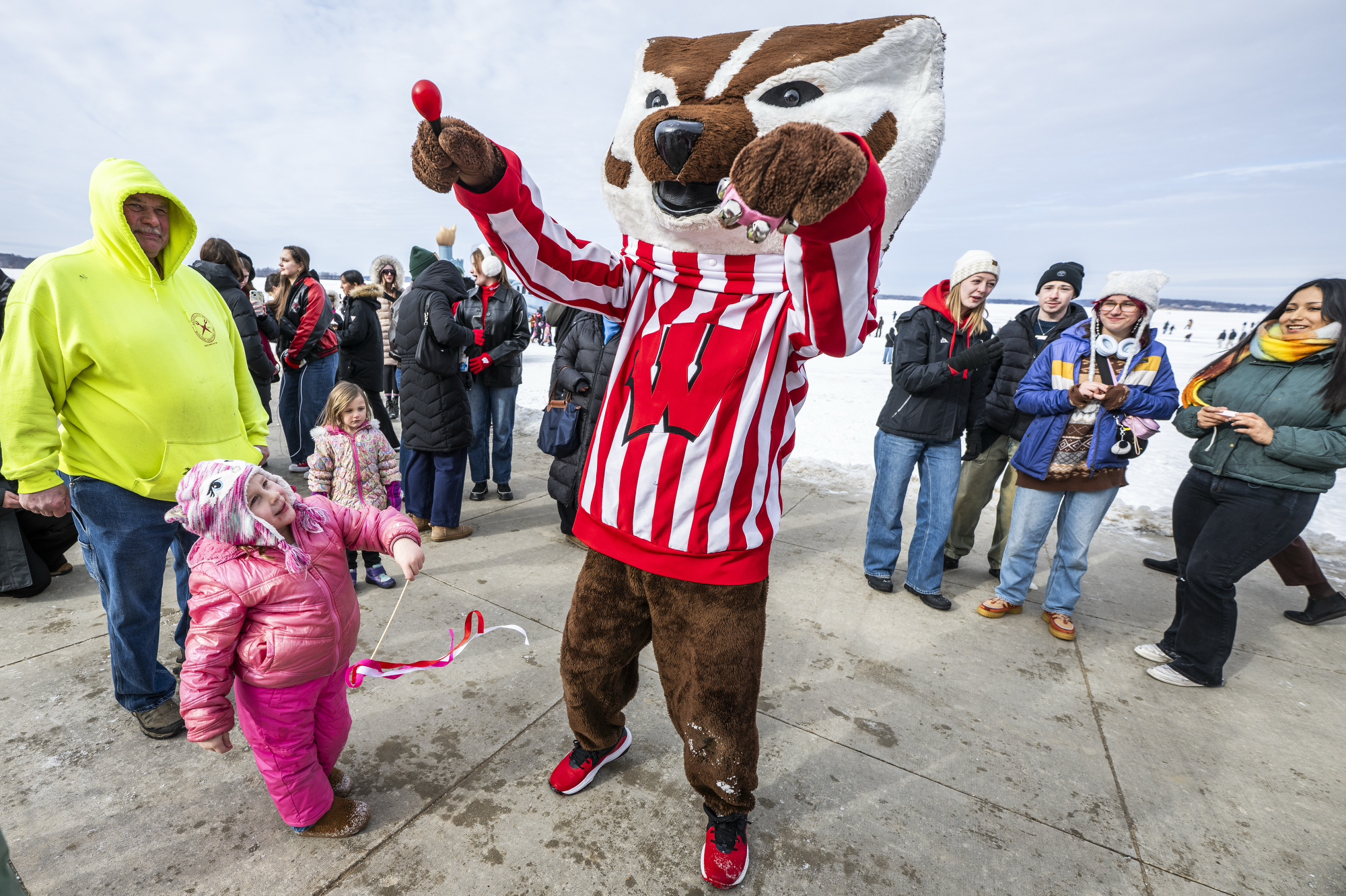 Bucky Badger dances with a small child as a crowd watches.