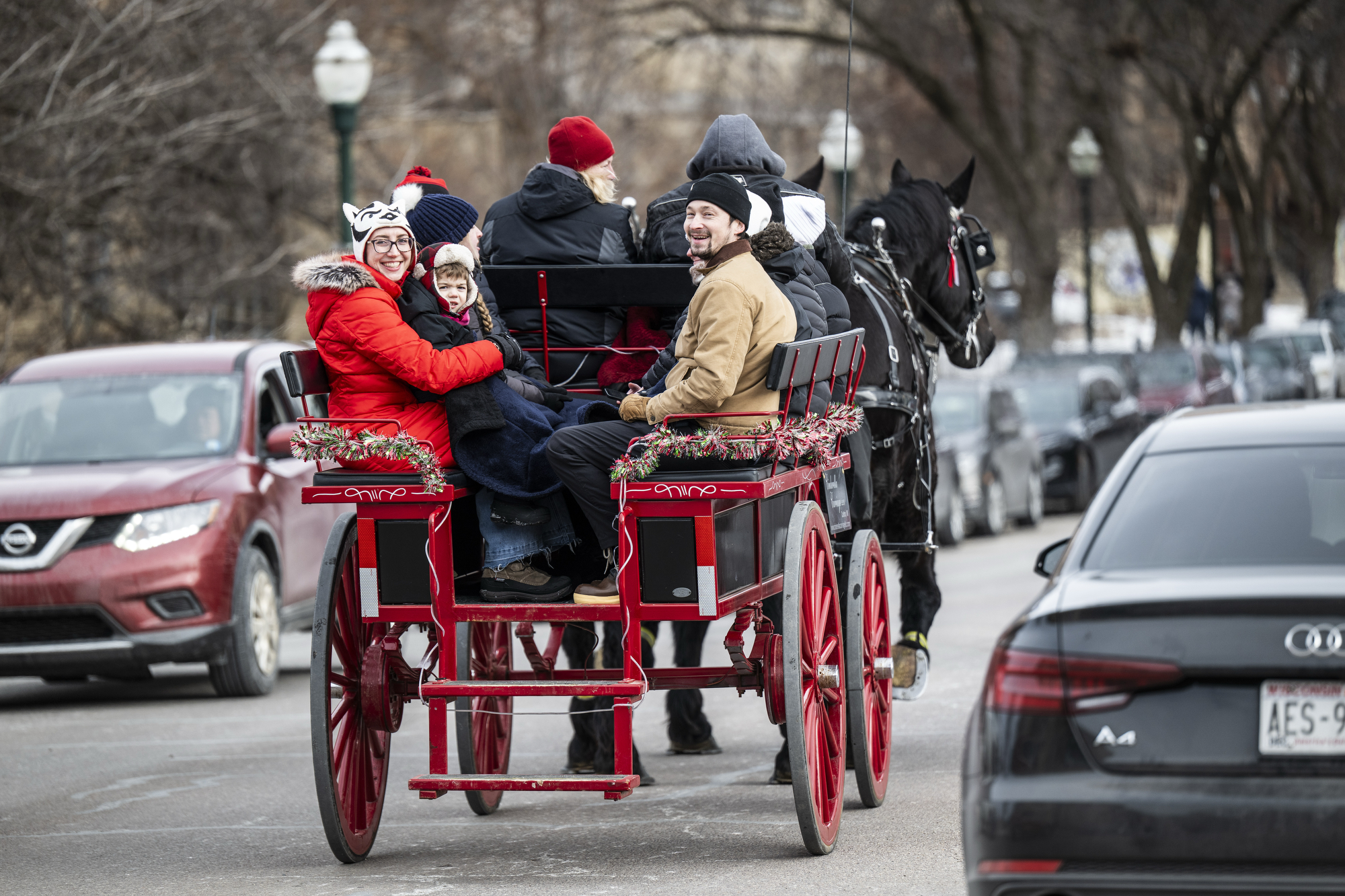 We see from behind people riding a red carriage down the street; a couple and their small child turn behind them to face and smile at the camera.