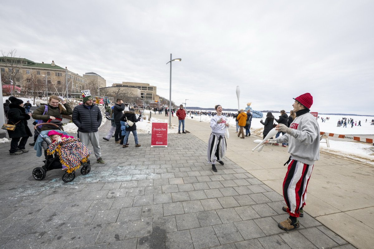 Two jugglers throw pins back and forth as a crowd watches.
