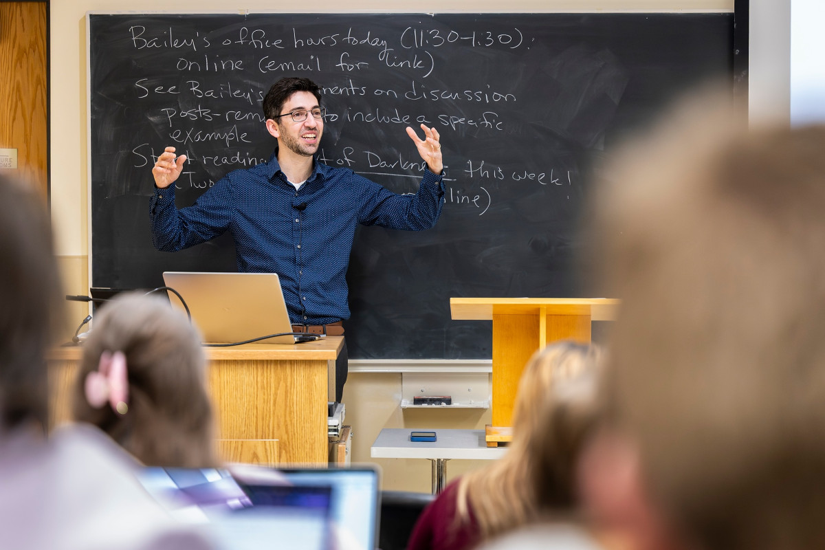 Brandon Bloch stands in behind a lectern in front of a large classroom speaking to his students.