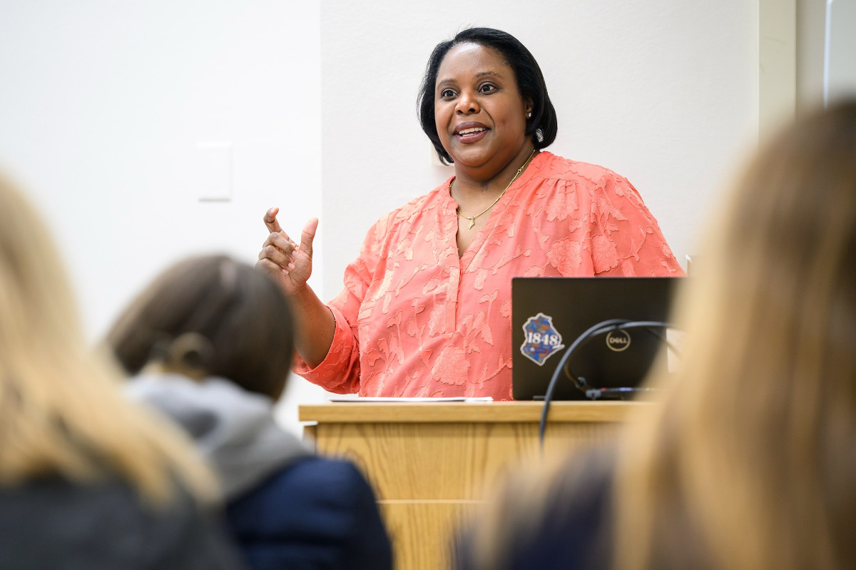 Christy Clark-Pujara stands in behind a lectern in front of a large classroom speaking to her students. 